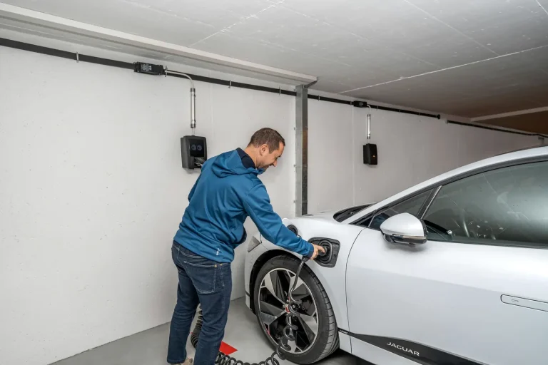 Homem conectando o carro elétrico ao carregador de parede na garagem