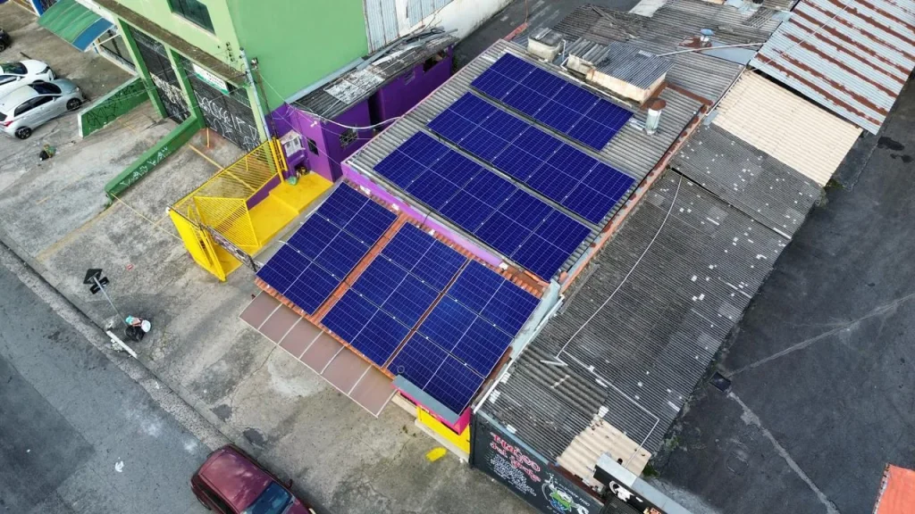 Placas solares sobre a cobertura de um comércio de rua, vistas por drone — obra da ORYGEN